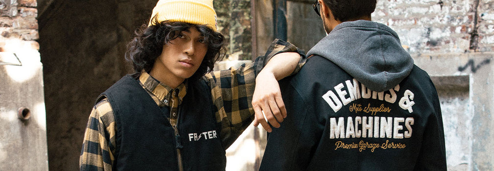 Dos personas con indumentaria Demons & Machines en look urbano workwear con campera y camisa a cuadros