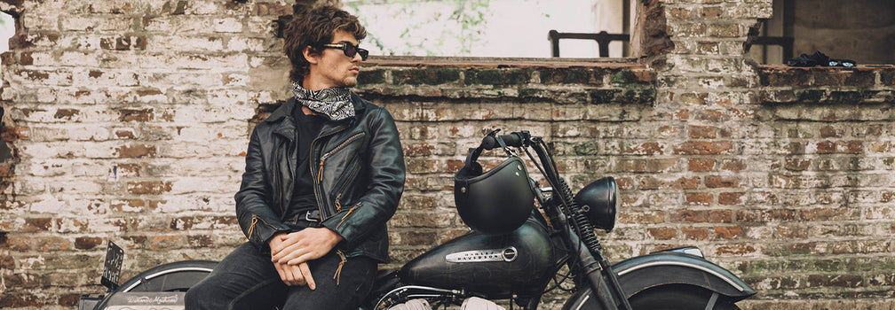 Modelo con campera de cuero Demons & Machines junto a moto en entorno urbano de estética industrial
