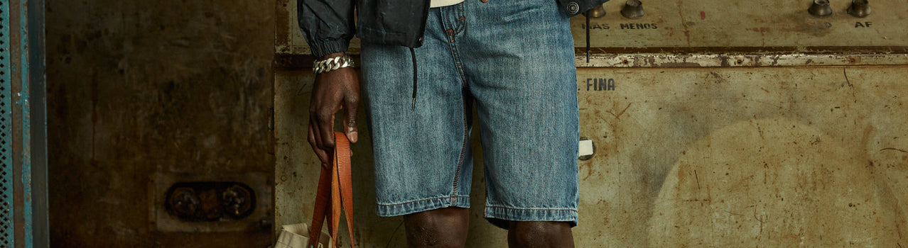 Bermuda de jean con cinturón y bolsa, frente a una pared envejecida — Bermudas