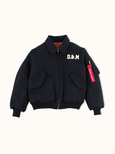 Campera Demons & Machines reversible estilo aviadora. Este estilo remite al modelo de camperas ALPHA, icónicas de la Fuerza Aérea por su diseño funcional para pilotos, caracterizadas por materiales resistentes, puños tejidos, bolsillos utilitarios y reversibilidad naranja para visibilidad en emergencias.
