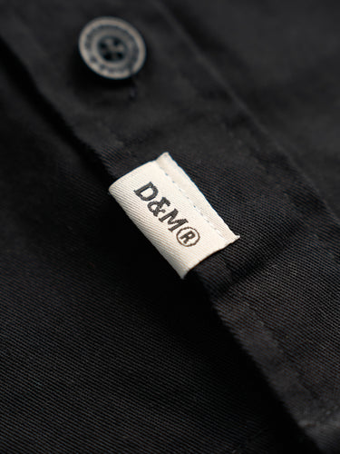Camisa Garage Boulder negra, detalle de la etiqueta D&M en la cartera. #color_negro