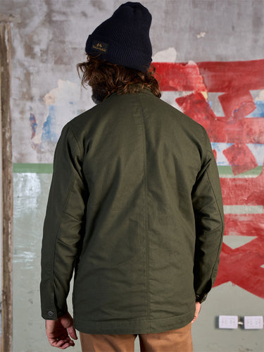Campera confeccionada en canvas pesado de algodón, con cuello en corderoy a contratono. Acceso frontal con cierre de metal oculto y mosquetones de metal a la vista. Este detalle está inspirado en los uniformes de los bomberos, sirven principalmente para cerrar de forma segura y rápida las prendas, garantizando que no se abran durante la emergencia, además de resistir altas temperaturas. #color_verde
