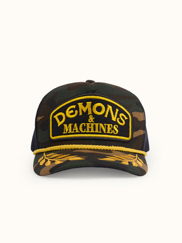 Gorra Podium de Demons & Machines en camuflaje, vista frontal mostrando el diseño y logotipo en la parte delantera.