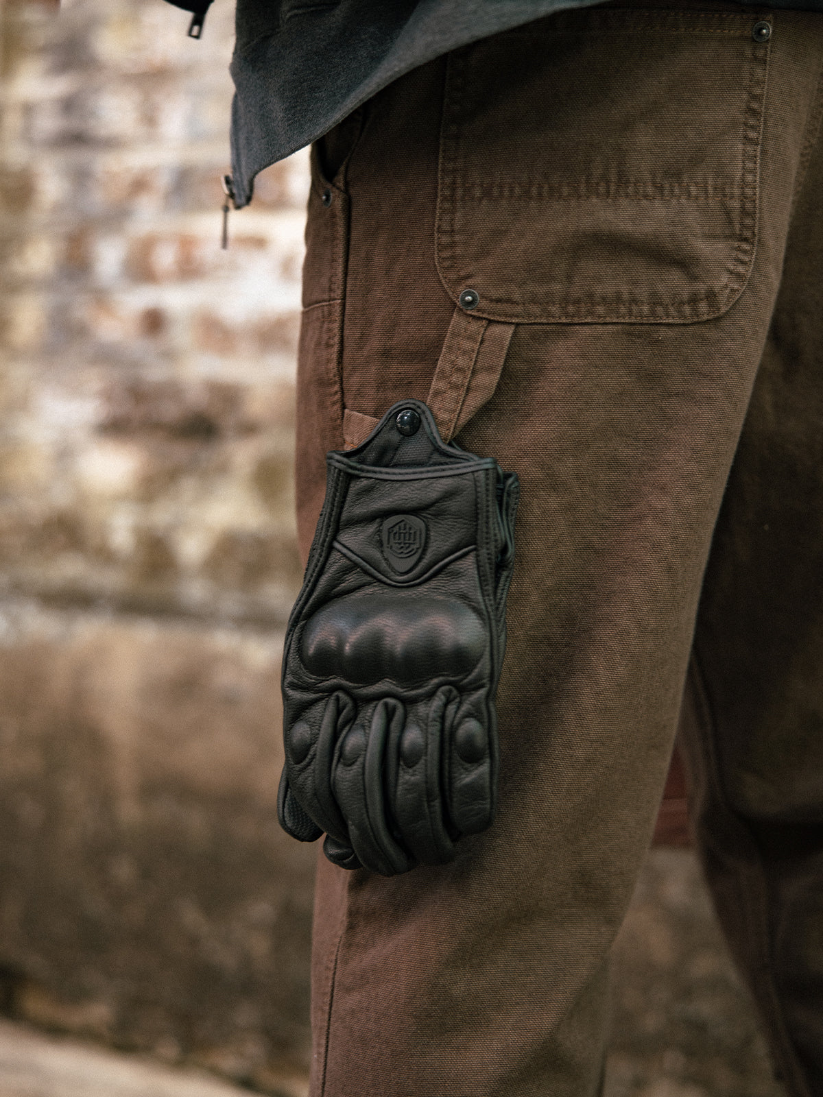 Guantes Redwood negros colgando del bolsillo de un pantalón de trabajo marrón, detalle con modelo