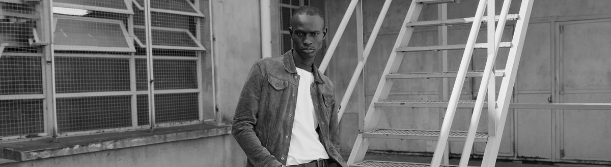 Hombre con campera oscura y remera blanca frente a una escalera metálica, en blanco y negro — Colección