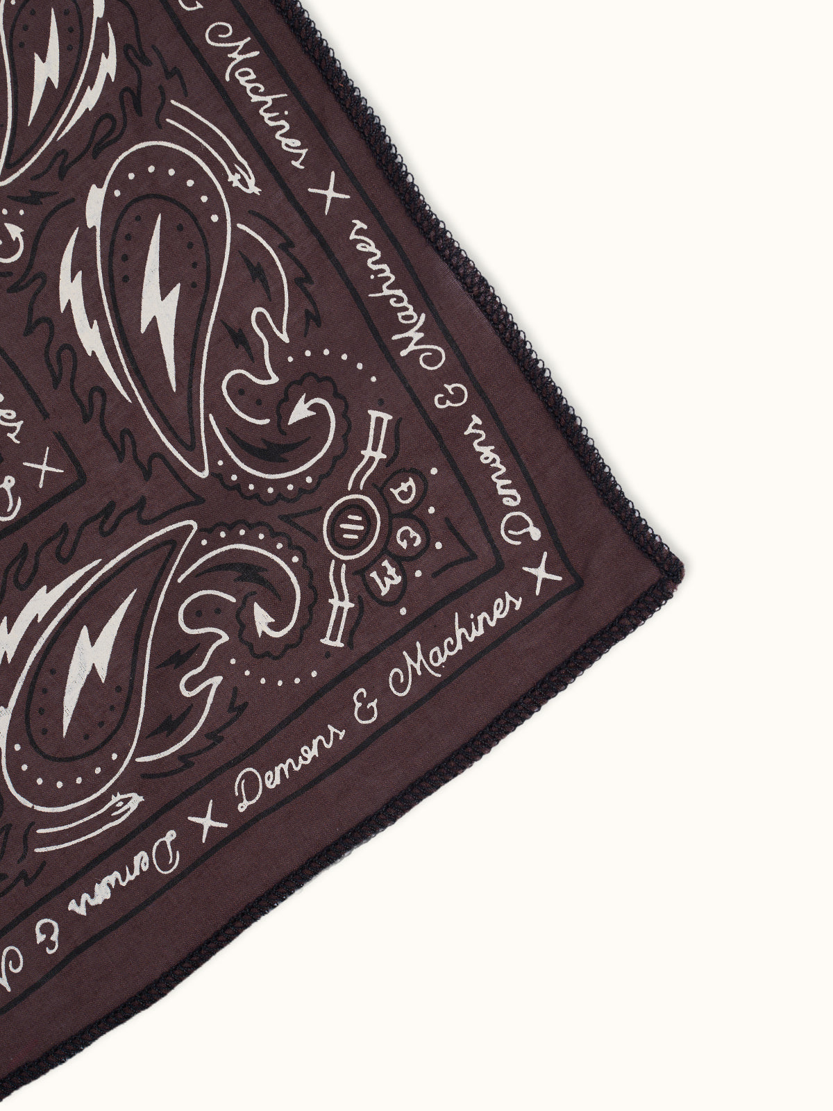 Detalle de la esquina del Pañuelo Traditional marrón con guarda paisley blanca y escudo DM