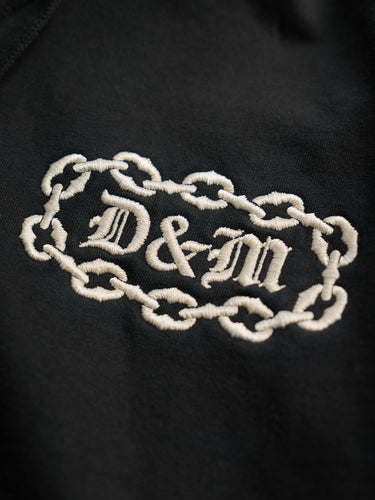 Buzo Hoodie Demons & Machines confeccionado en rústico de algodón de buen peso, con puños tejidos en morley al tono en mangas y bajo ruedo. Capucha ajustable mediante cordón. Bordados marcarios en altura 3D con hilo a contratono. 100% Algodón.   #color_negro