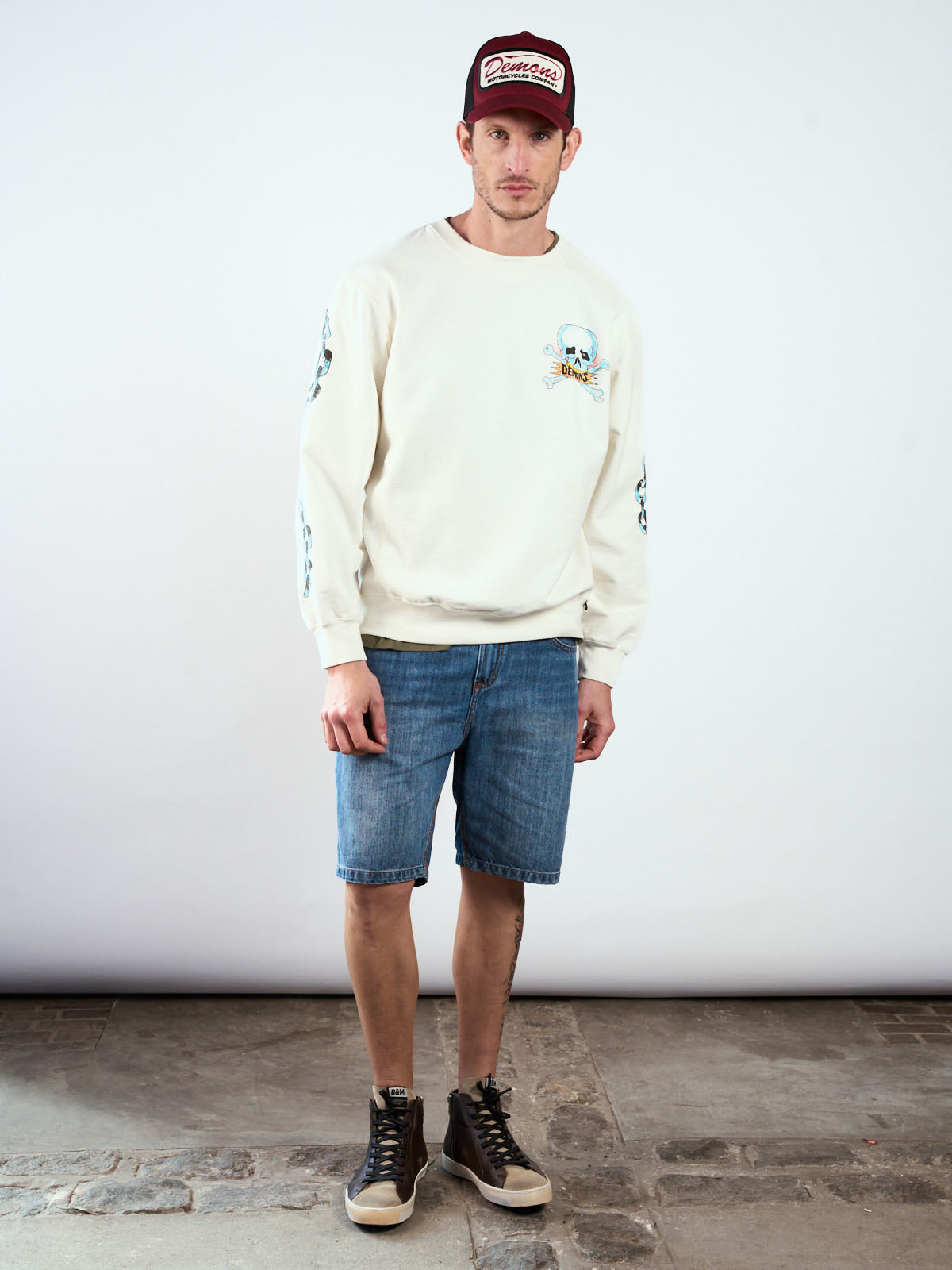 Bermuda Alex Mid Blue puesta, cuerpo entero con buzo crudo, gorra trucker y zapatillas altas #color_azul