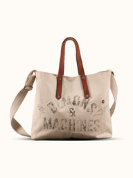 Bolso Demons & Machines estilo tote confeccionado artesanalmente en lona pesada de algodón, con manija en cuero vacuno 100% y correa reforzada de algodón regulable. Herrajes metálicos en baño cobre empavonado oxidados artesanalmente. Cuenta con dos bolsillos internos. Logo de marca estampado en serigrafía con efecto gastado y roto. #color_crudo