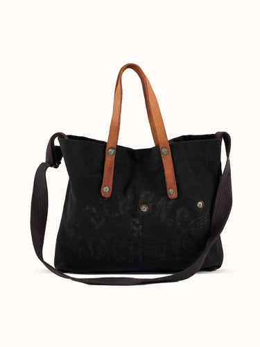 Bolso Demons & Machines estilo tote confeccionado artesanalmente en lona pesada de algodón, con manija en cuero vacuno 100% y correa reforzada de algodón regulable. Herrajes metálicos en baño cobre empavonado oxidados artesanalmente. Cuenta con dos bolsillos internos. Logo de marca estampado en serigrafía con efecto gastado y roto. #color_negro
