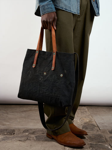 Bolso Demons & Machines estilo tote confeccionado artesanalmente en lona pesada de algodón, con manija en cuero vacuno 100% y correa reforzada de algodón regulable. Herrajes metálicos en baño cobre empavonado oxidados artesanalmente. Cuenta con dos bolsillos internos. Logo de marca estampado en serigrafía con efecto gastado y roto. #color_negro