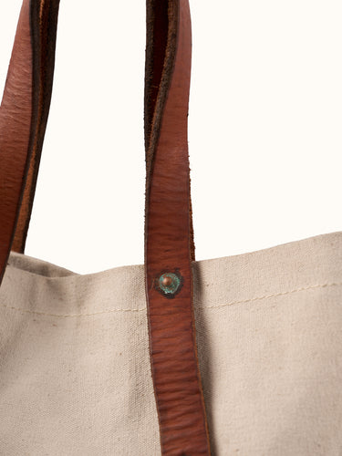 Bolso Demons & Machines estilo tote confeccionado artesanalmente en lona pesada de algodón, con manija en cuero vacuno 100% y correa reforzada de algodón regulable. Herrajes metálicos en baño cobre empavonado oxidados artesanalmente. Cuenta con dos bolsillos internos. Logo de marca estampado en serigrafía con efecto gastado y roto. #color_crudo