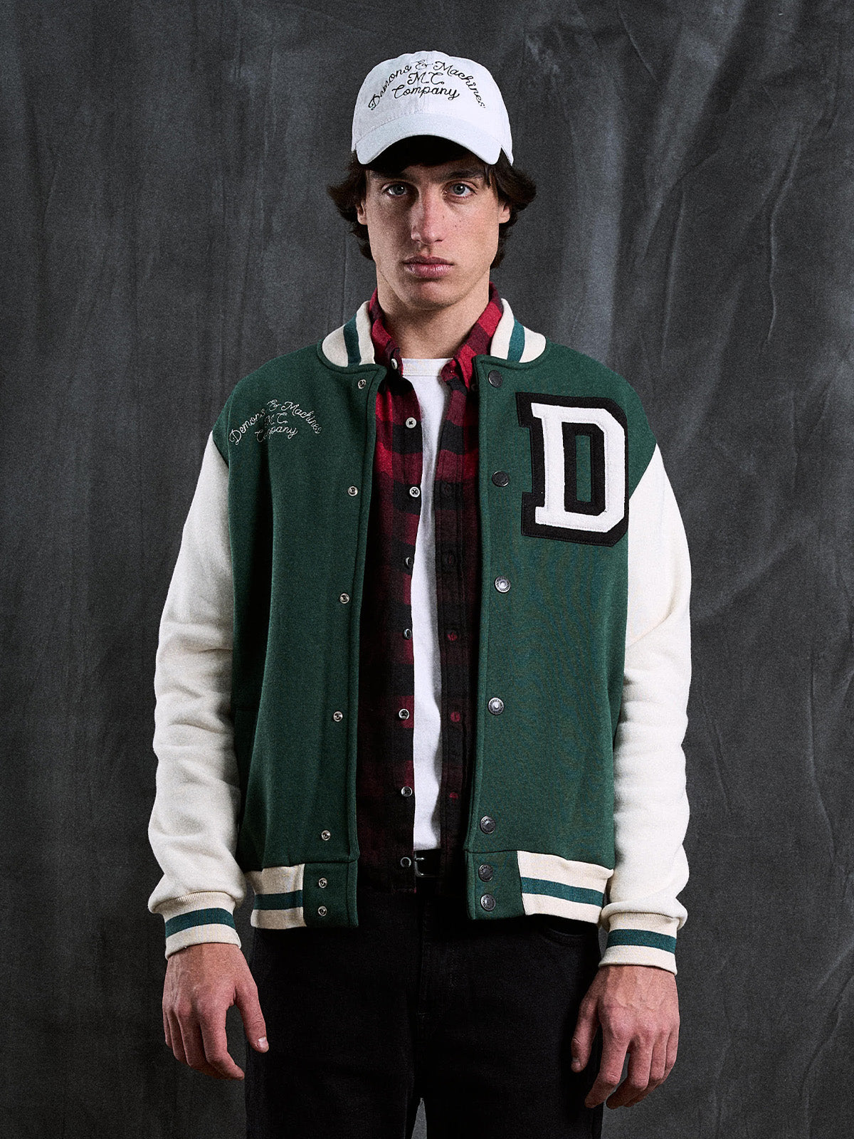 Campera Stanford verde puesta, vista de frente con camisa a cuadros, gorra blanca y fondo gris texturado #color_verde