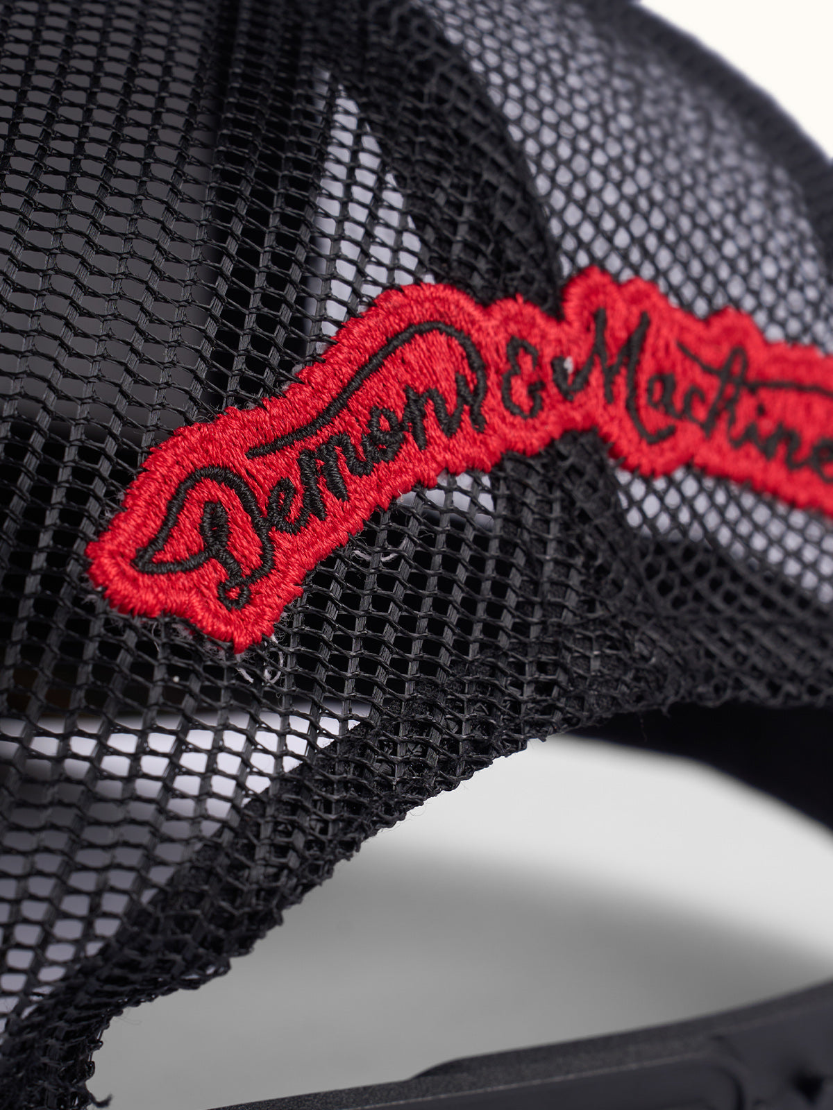 Primer plano del bordado Demons & Machines en cursiva roja sobre la red de la Gorra Trucker camuflada