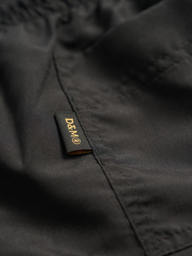 Short de baño Demons & Machines confeccionado en microfibra mate. Bolsillos laterales, cintura elastizada con cordón ajustable y logo bordado al tono. #color_negro