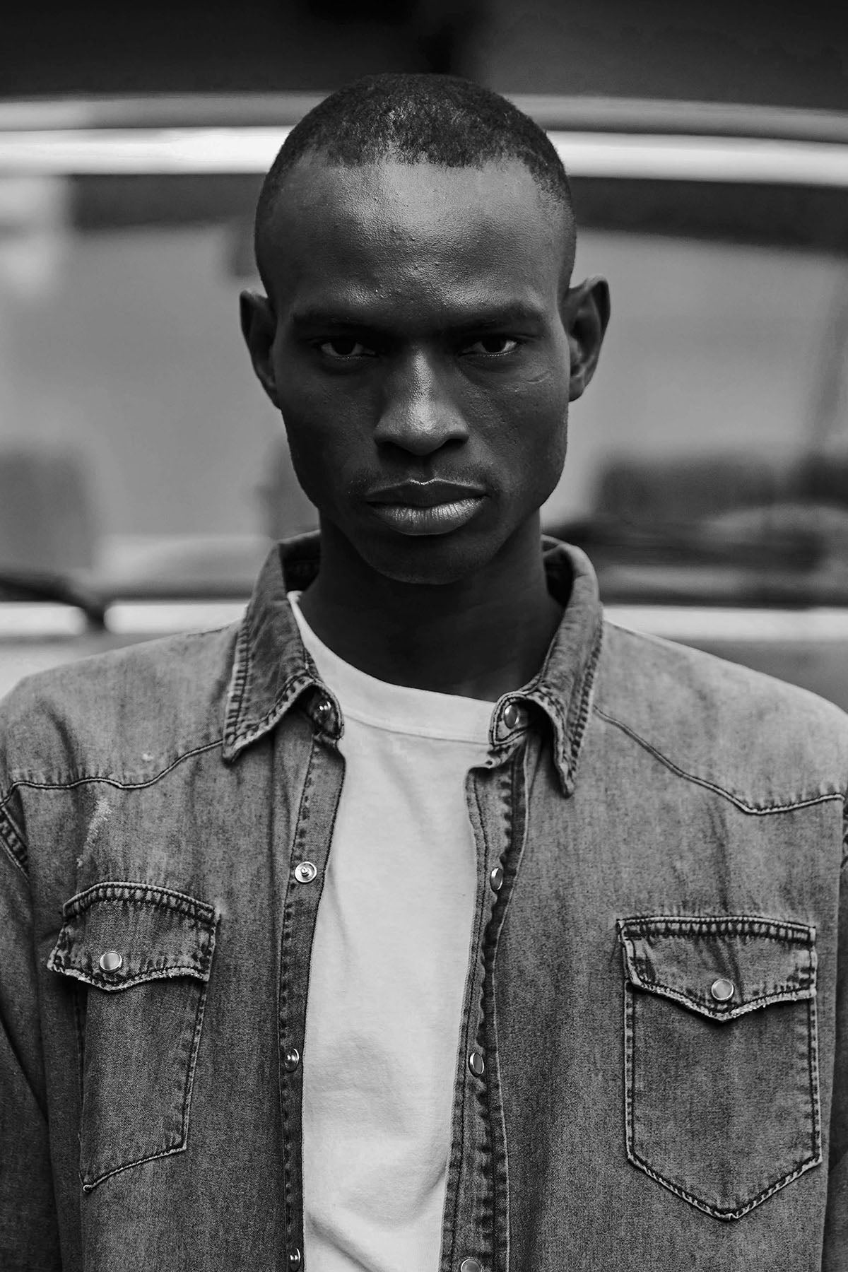 Hombre con camisa de jean gris abierta sobre remera blanca, retrato en blanco y negro