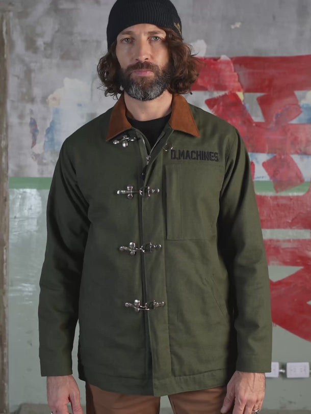 Campera confeccionada en canvas pesado de algodón, con cuello en corderoy a contratono.  Acceso frontal con cierre de metal oculto y mosquetones de metal a la vista. Este detalle está inspirado en los uniformes de los bomberos, sirven principalmente para cerrar de forma segura y rápida las prendas, garantizando que no se abran durante la emergencia, además de resistir altas temperaturas. #color_verde