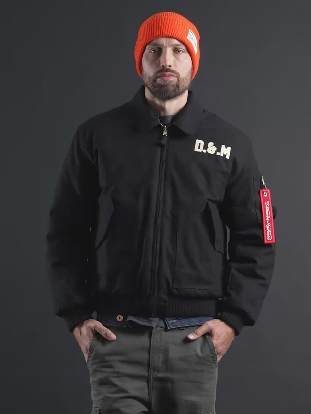 Campera Demons & Machines reversible estilo aviadora. Este estilo remite al modelo de camperas ALPHA, icónicas de la Fuerza Aérea por su diseño funcional para pilotos, caracterizadas por materiales resistentes, puños tejidos, bolsillos utilitarios y reversibilidad naranja para visibilidad en emergencias.
