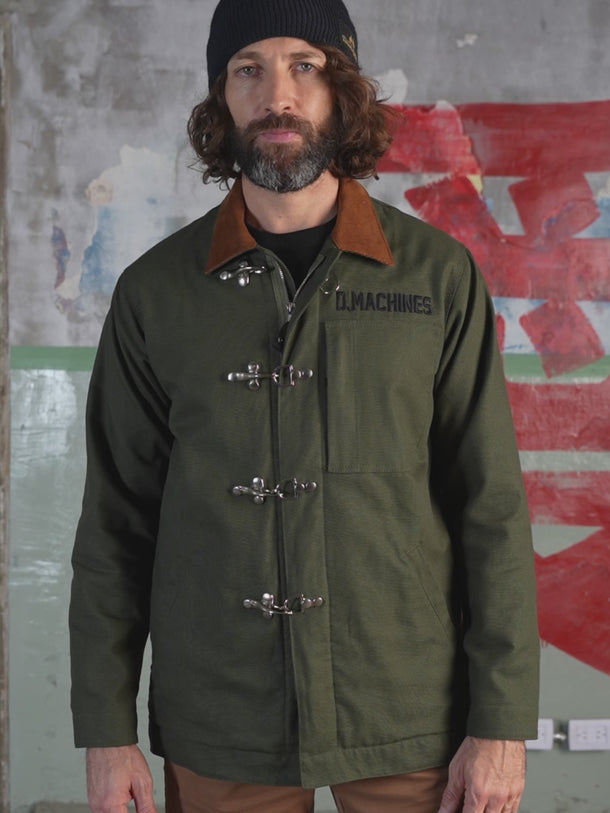 Campera confeccionada en canvas pesado de algodón, con cuello en corderoy a contratono.  Acceso frontal con cierre de metal oculto y mosquetones de metal a la vista. Este detalle está inspirado en los uniformes de los bomberos, sirven principalmente para cerrar de forma segura y rápida las prendas, garantizando que no se abran durante la emergencia, además de resistir altas temperaturas. #color_verde