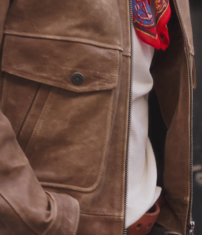 Video: campera de cuero marrón envejecido con cierre metálico, pañuelo rojo estampado y remera blanca, en detalle
