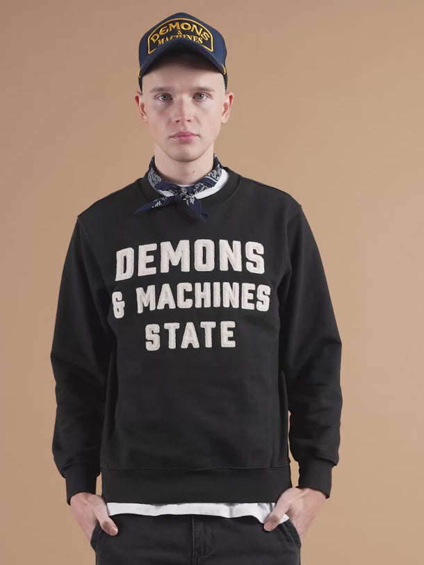 Buzo Demons & Machines cuello redondo de calce slim, con complemento morley en cuello, puños, bajo ruedo y laterales. Bordado marcaría al frente, con letras aplicadas en paño y pespuntes al tono. Suavizado sobre prenda terminada.