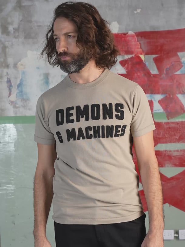 Remera Demons & Machines manga corta confeccionada en Jersey 16/1 de algodón peinado. Calce slim y cuello terminado en collareta con complemento ribb. Terminaciones de mangas y ruedo en dobladillo con costura india. Bordado marcaría al frente, con letras aplicadas en paño y pespuntes al tono. Suavizado sobre prenda terminada.#color_khaki